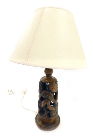 An African carved hardwood tribal table lamp base, decorated with figures, etc., and a cream shade, 62cm high overall.