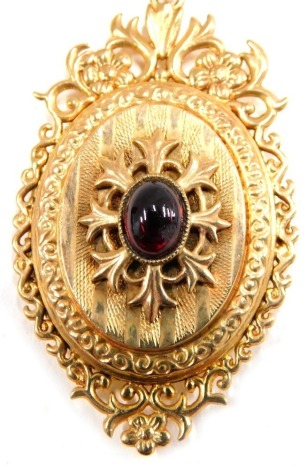 An Edwardian 9ct gold pendant and chain, the oval locket set with cabochon ruby, with scroll and engine turned decoration, inset with watch links, 4.5cm high, on a curb link chain, yellow metal unmarked, 50cm long, 15.8g all in.