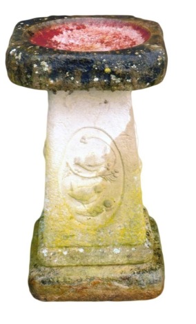 A reconstituted stone bird table, the square design top on a column decorated with birds and berries, 62cm high, the top 36cm x 36cm.