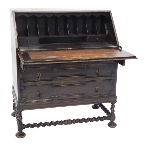 A 1920s oak bureau, with panelled fall enclosing a fitted interior above three graduated panelled drawers, on spirally turned supports and stretchers with pad feet, 90cm wide.