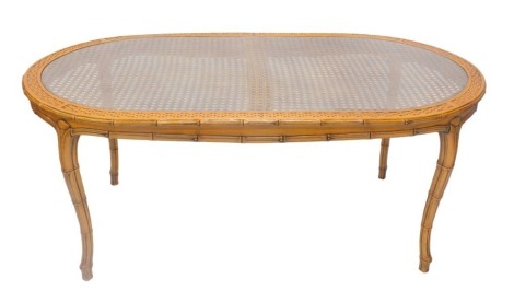 A faux bamboo and raffia oval dining table, with glass top, 180cm x 100cm.