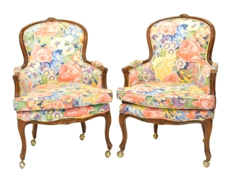 A pair of walnut French style armchairs, each upholstered in bright floral fabric on cabriole legs, with castors. The upholstery in this lot does not comply with the 1988 (Fire & Fire Furnishing) Regulations, unless sold to a known exporter or upholstere