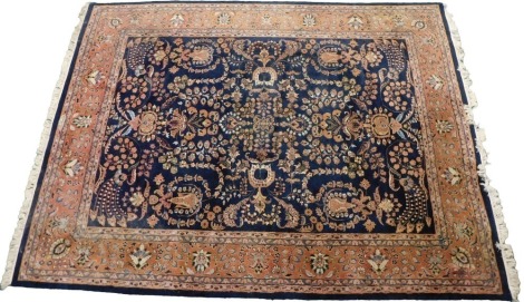 An Indian Serapi design wool rug, decorated overall with flowers, medallions, scrolls, etc., in multiple colours, on a navy ground, one wide and two narrow borders, 370cm x 284cm.