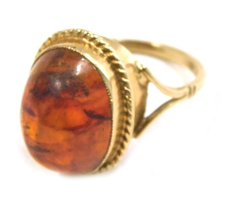 A 9ct gold imitation amber dress ring, the raised polished cabochon amber style stone in a rope twist setting on V splayed shoulders, ring size O½, 4.3g all in.