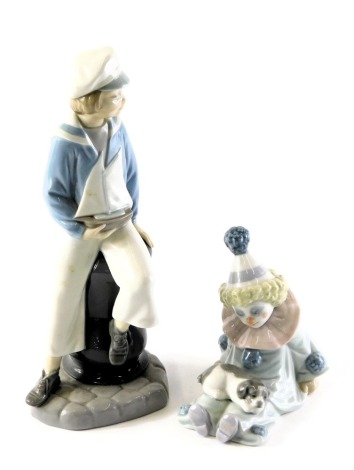 Two Lladro porcelain figures, modelled as a young boy seated holding pond yacht, printed marks, 24cm high, and a seated clown figure with puppy in lap, 12cm high.