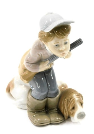 A Lladro porcelain figure group modelled as a young boy crouching holding gun beside hound, printed marks, 19cm high.