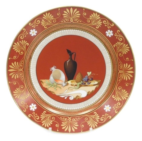 A mid 19thC Sevres Etruscan red ground hard paste porcelain dessert plate, decorated with a still life of wine cup, flagon and bowl of fruit, within a stylised gilt anthemion leaf and scroll border, Napoleon crowned 'N' mark in iron red, 24cm diameter. Au