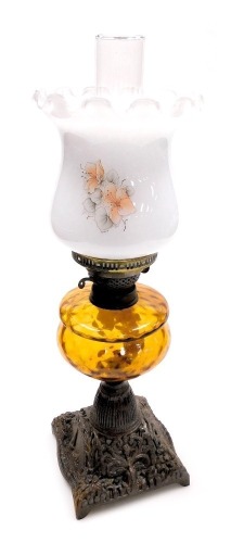 An early 20thC oil lamp, with an opaque shade, decorated with flowers, an amber glass central reservoir, on a cast iron base, with chimney, 58cm high.