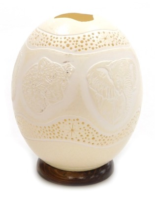 An ostrich egg night light, carved with wild animals, within pierced star and dot borders, on a turned wooden base, 18cm high.