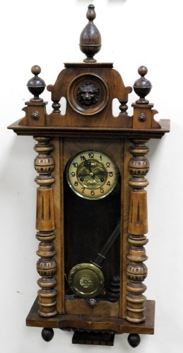 A late 19thC Vienna mahogany cased wall clock, circular brass dial embossed with flowers, chapter ring bearing Arabic numerals, eight day movement with coil strike, the triple urn topped pediment carved centrally with a lion's head mask, the case with arc