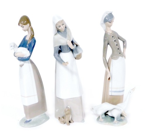 Three Lladro porcelain figures, comprising a lady with a puppy at her feet, and a basket of loaves 27.5cm high, a girl holding a lamb, 26.5cm high, and a lady with geese, 27.5cm high. (3)