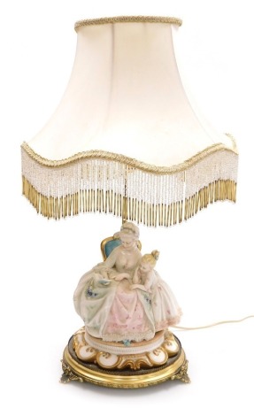 A Capodimonte porcelain figural table lamp, modelled as an 18thC lady seated reading a book to a child, raised on a Rococo style base, above a circular brass stand on three leaf scroll feet, with frilled cream shade, 55cm high.