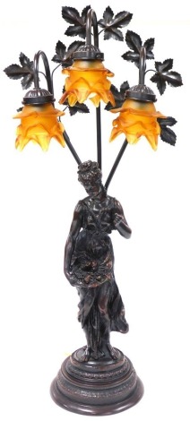 An Art Nouveau style bronzed plaster figural table lamp, modelled as a lady with a bowl of fruit, standing on a tiered circular base, with three frosted amber glass shades, 83.5cm high.