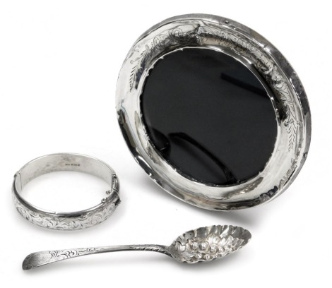 A George III silver berry spoon, the bowl embossed with a leaf and berries, with an engraved handle together with a silver bangle, with foliate engraved decoration, on a snap clasp, with safety chain as fitted, and a George V silver strut photograph frame