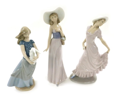 Three Nao porcelain figures of young ladies, one in a pink dress, another holding a rabbit, the third with a basket of flowers, printed marks. (AF)