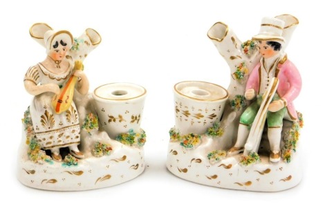 A pair of late 19thC Staffordshire pottery inkwells, modelled with a seated man playing a harp, a lady playing a lute, seated behind a two branch tree stump, with a well alongside, raised on an oval base, 11cm high.