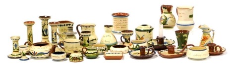 A group of Devon Motto Ware pottery, including candlesticks, hair tidy, chamber sticks, tea cup and saucer, jugs and egg cups. (qty)