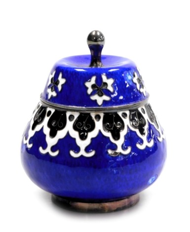 A Continental enamel pot and cover, decorated in black and white with flowers and stylised leaves against a blue ground, set in white metal, stamped silver, 6.32oz all in, 9cm high. (AF)