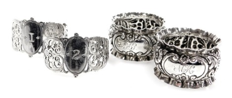 A pair of Victorian silver napkin rings, with pierced and foliate decoration, with oval reserves numbered 1 and 2, Sheffield 1896, and a further pair of Victorian napkin rings, with embossed floral and foliate decoration, central reserve monogram engraved