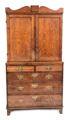 A George III oak linen press, with a shaped pediment over a pair of panelled doors enclosing shelves, above two short over three long graduated drawers, raised on bracket feet, 203cm high, 109cm wide, 51cm deep.