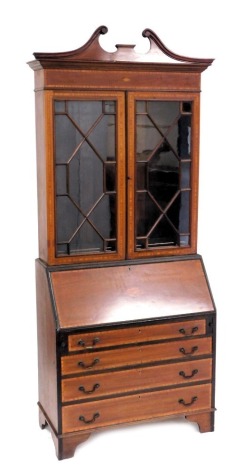 An Edwardian mahogany bureau bookcase, with satinwood cross banding, and shell paterae inlay, the break arch pediment over a pair of astragal glazed doors, enclosing three shelves, above a fall flap opening to reveal a central door flanked by six recesses