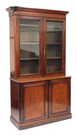 A Victorian mahogany cupboard bookcase, the outswept pediment above a pair of glazed doors enclosing three shelves, over a pair of panelled doors enclosing two further shelves, raised on a plinth base, 229cm high, 124cm wide, 52.5cm deep.