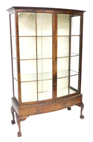 An early 20thC mahogany bow front display cabinet, the outswept pediment over a pair of astragal glazed doors, enclosing three glass shelves, raised on foliate carved cabriole legs and ball and claw feet, 179cm high, 115cm wide, 47.5cm deep.