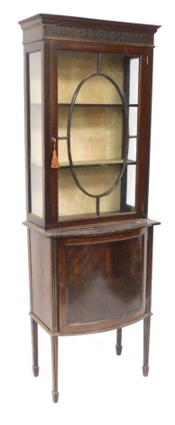 A Victorian mahogany cupboard display cabinet, the pediment above a blind fretwork frieze, over a glazed door enclosing two shelves, above a bow fronted cupboard, raised on channeled square legs on splayed feet, 185cm high, 64cm wide, 36cm deep.