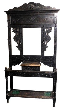 A Victorian ebonised hall stand, with a lion's head carved crest rail, above a central mirror, inset bevelled glass, flanked by carved phoenixes, over a glove box and base with two umbrella drip trays, raised on turned supports, 212cm high, 104cm wide, 31