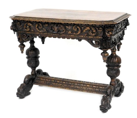 A Victorian oak library table, with a foliate carved and canted rectangular top, above a foliate carved frieze, with single long drawer, and lion's head carved corners, above a foliate and acorn carved apron, raised on fluted and leaf carved cup and cover