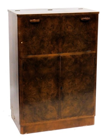 A mid century Art Deco walnut cocktail cabinet, the cantilevered top and drop front opening to reveal a glass back and bottom fitted interior, bearing label for Gold Feather Products, over a pair of cupboard doors enclosing a single shelf, raised on a pli