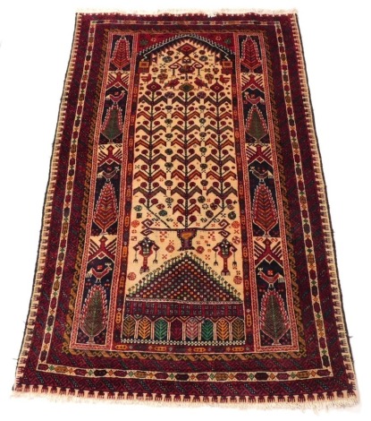 A Baluch prayer rug, the cream ground mihrab filled with a tree of life, birds and flowers, within a frame of trees and birds, and repeating geometric borders, 175cm x 107cm.