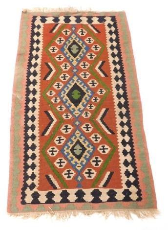 A Turkish kilim rug, the central red field decorated with three blue medallions, chevrons and other motifs, within repeating geometric borders, 164cm x 98cm.