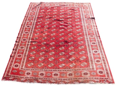 A Bokhara red ground rug, the central rectangular field decorated with repeating floral medallions, within repeating floral borders, 327cm x 268cm.