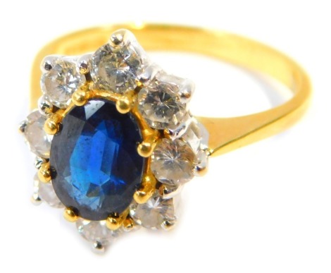 An 18ct gold, sapphire and diamond cluster ring, with oval set sapphire, 7.8mm x 5.6mm x 2.6mm, in eight claw setting, surrounded by eight round brilliant cut diamonds, each approx 0.10ct, in a white and yellow gold setting, on a yellow metal band, hallma