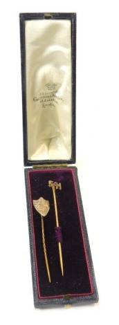 Two stick pins, comprising a shield pin with maple leaf design, yellow metal top unmarked, on brass pin, and another plated example stamped 541, in Goldsmith and Jewellers Durrant of London box. (2)