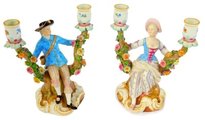 A pair of late 19thC Meissen porcelain candelabra, modelled as a gallant and lady, seated within a tree, encrusted with flowers, raised on a rococo scroll base, incised numbers 1129 and 1130, painted marks, 20cm high.