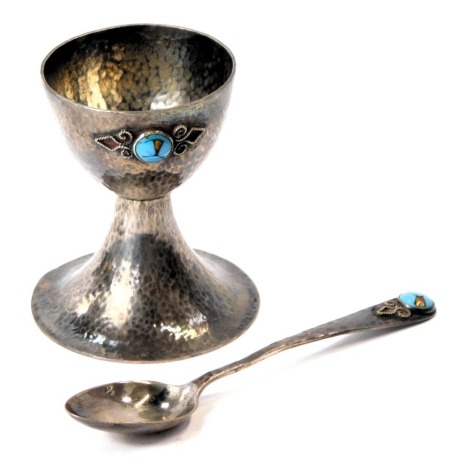 An Arts and Crafts hammered silver egg cup and spoon, the body of hammered design with scroll applied detail and set with turquoise, maker BI, Birmingham 1926, 2.74oz, in fitted case.