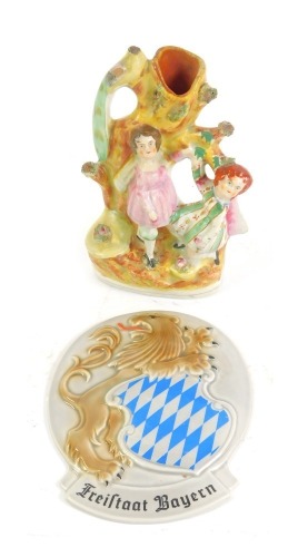 A late 19thC Staffordshire pottery spill vase, depicting a peacock on a tree, with children playing below, 20cm high, and a Goebel Freisstaat porcelain plaque, 18cm high. (2)