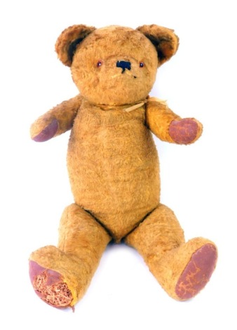 An early 20thC plush blonde jointed straw filled Teddy bear, with amber glass eyes, and pad paws and feet, 55cm high. (AF)