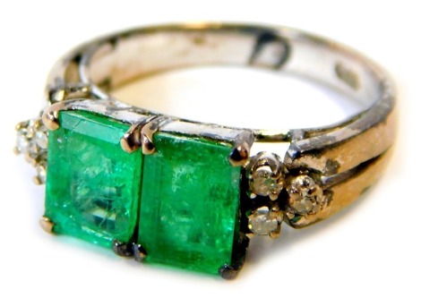 An emerald and diamond dress ring, set with two rectangular cut emeralds, each in four claw setting, 7.2mm x 5.2mm x 3mm, flanked by three tiny diamonds to each shoulder, on V splayed shoulders, on a white gold band stamped 18k, ring size N, 4.2g all in.