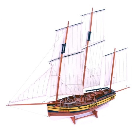 A model of a three masted sailing vessel, wooden hull, fully rigged with sails, on a black and yellow ribbed border, 64cm high, 82cm wide.