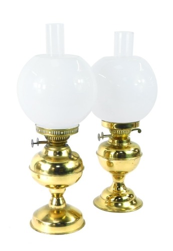 Two brass oil lamps, each with a white shade and funnel on circular foot, 51cm high. (2)