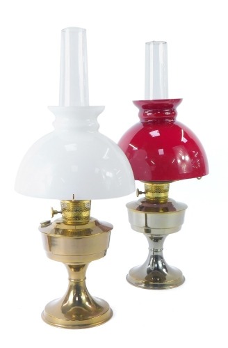 Two oil lamps, comprising one with red flash glass shade and funnel, on chrome finish base, 62cm high, and another with white finish shade, 63cm high. (2)