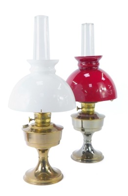 Two oil lamps, comprising one with red flash glass shade and funnel, on chrome finish base, 62cm high, and another with white finish shade, 63cm high. (2)