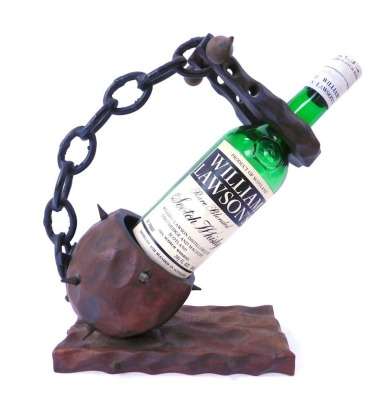 A carved wooden Flai wine bottle stand, the spike ball applied with chain, on a rectangular base, with William Lawson's empty whisky bottle, 31cm high, 25cm wide.