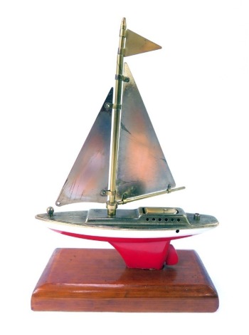 A mid century novelty boat table lighter, with brass sail, red and white painted hull, on a rectangular pine base, 22cm high.