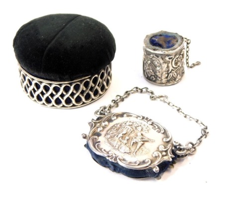 An early 20thC silver pin cushion box, the black velvet overstuffed lid opening to reveal a blue satin interior, the outer silver border of pierced decoration in infinity knots, Birmingham 1907, 6cm diameter, together with a silver pin cushion, decorated 