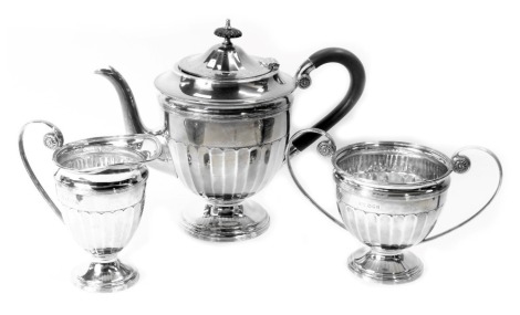 A George V silver tea service, comprising teapot, milk jug and sugar bowl, each of Neoclassical design with scroll arched handles, ebonised handle and knop to teapot, on a fluted body, maker CWF, London 1921, 37.53oz gross. (3)