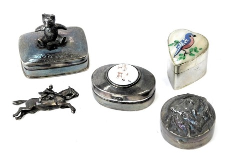 Four white metal pill boxes, comprising one with articulated bear to top, another with transfer printed semi clad female figure, another with dog and pheasant, grouse, white metal stamped Sterling, an unmarked plated love heart shaped pill box, and a whit